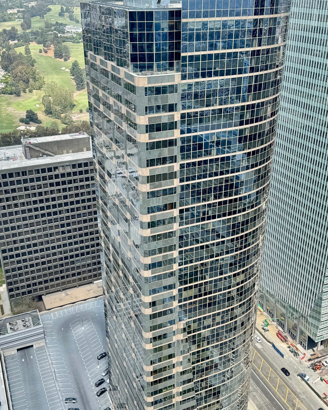 High-rise glass office building in cityscape, photographed from above during the day.