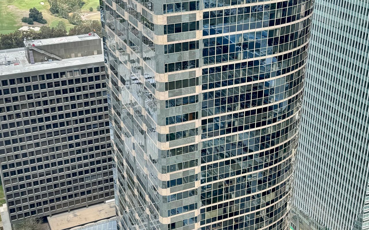 High-rise glass office building in cityscape, photographed from above during the day.