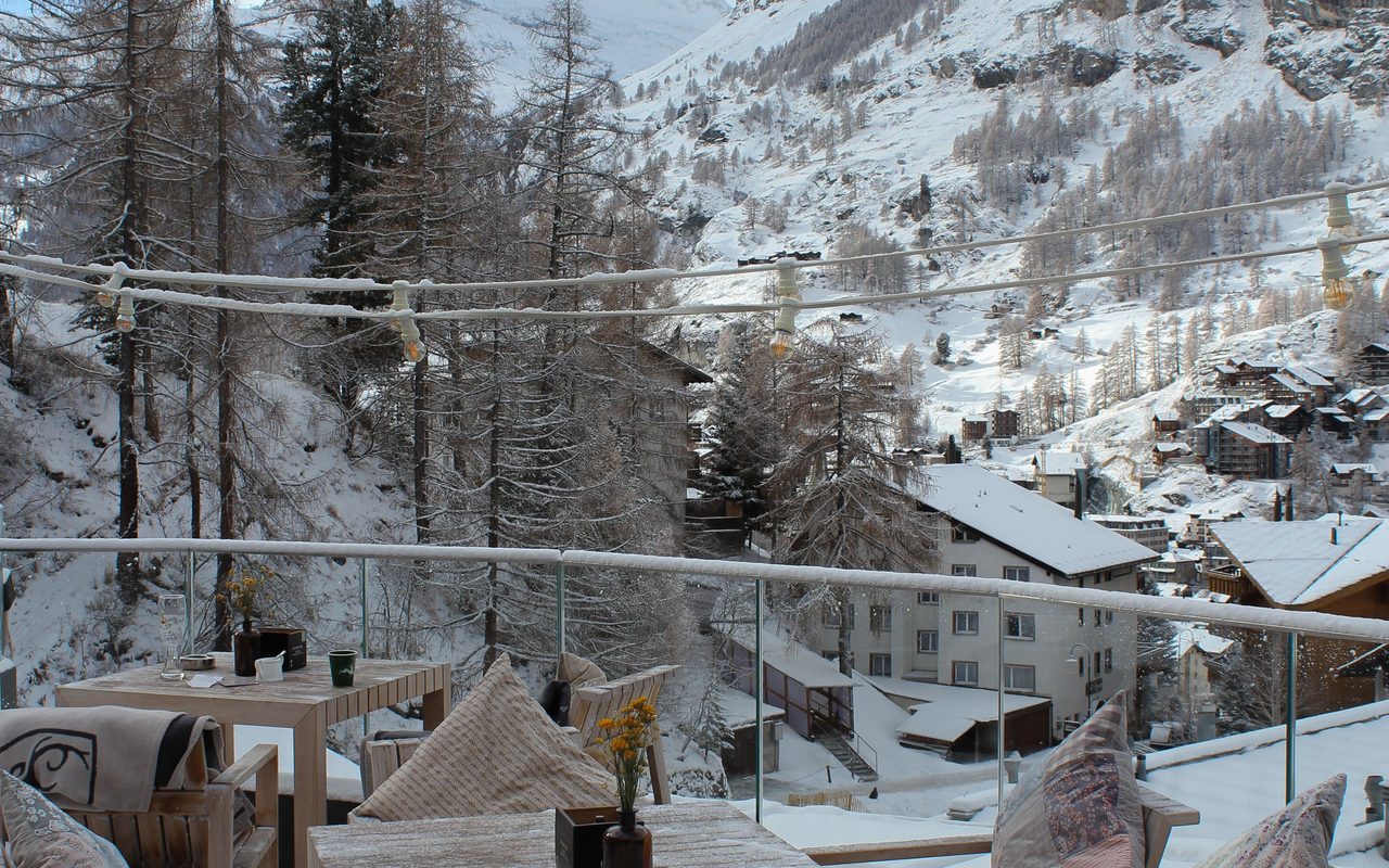 Timber mountain-retreat terrace with glass balustrade and snow-covered Alpine peaks