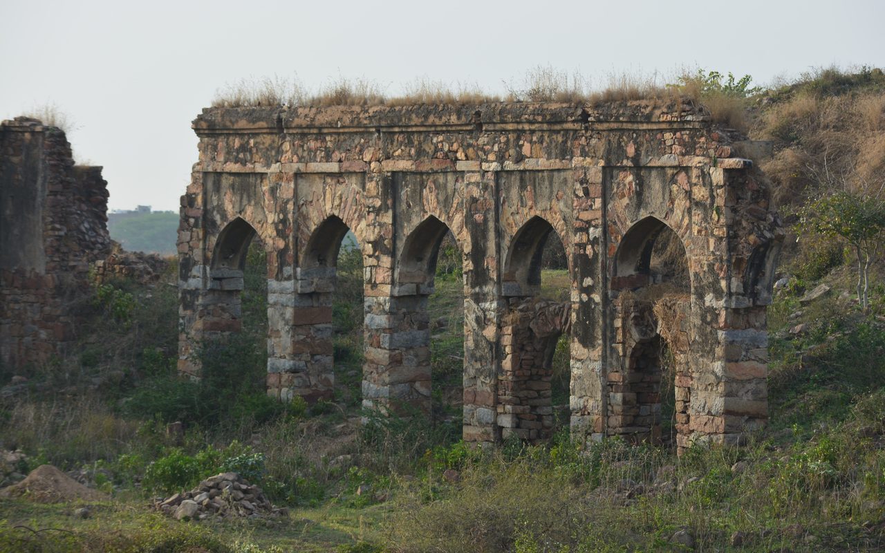Beautiful archway ruins of Tughlaqabad Fort in New Delhi, showcasing ancient architecture amidst greenery.