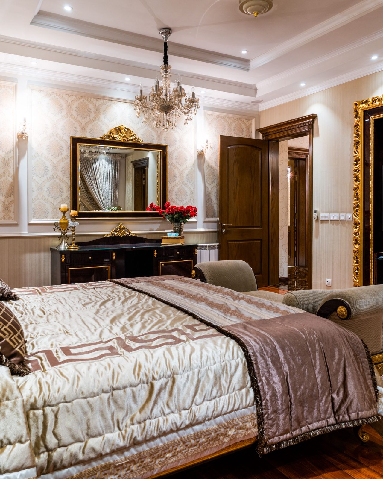 Luxurious hotel bedroom featuring elegant decor, large mirror, chandelier, and gold accents.