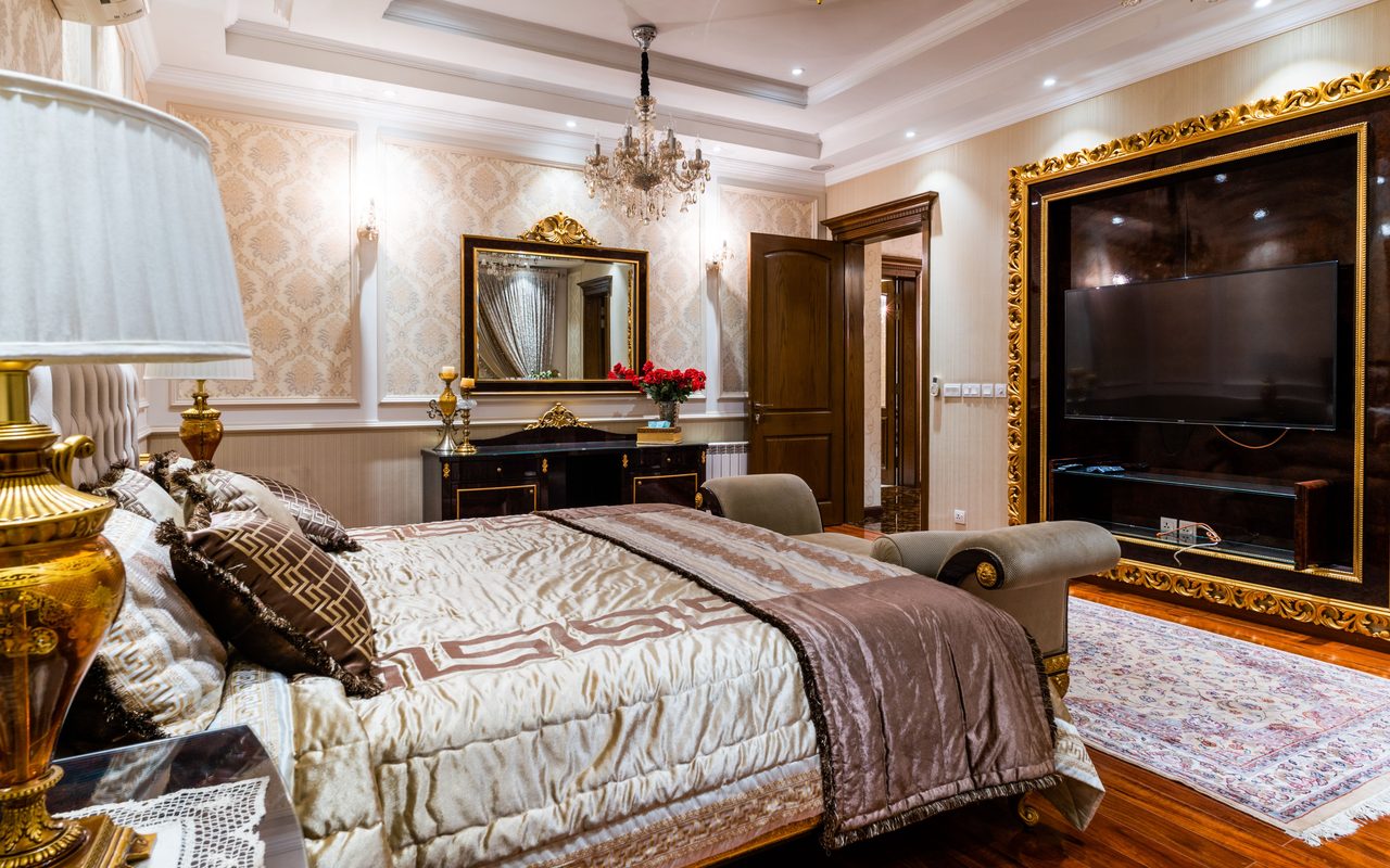 Luxurious hotel bedroom featuring elegant decor, large mirror, chandelier, and gold accents.