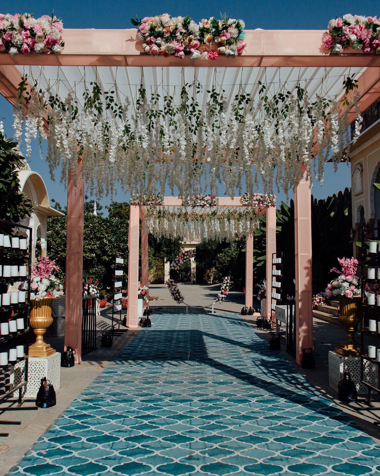 Beautiful outdoor wedding aisle with pink floral arches and a patterned path under clear sky.