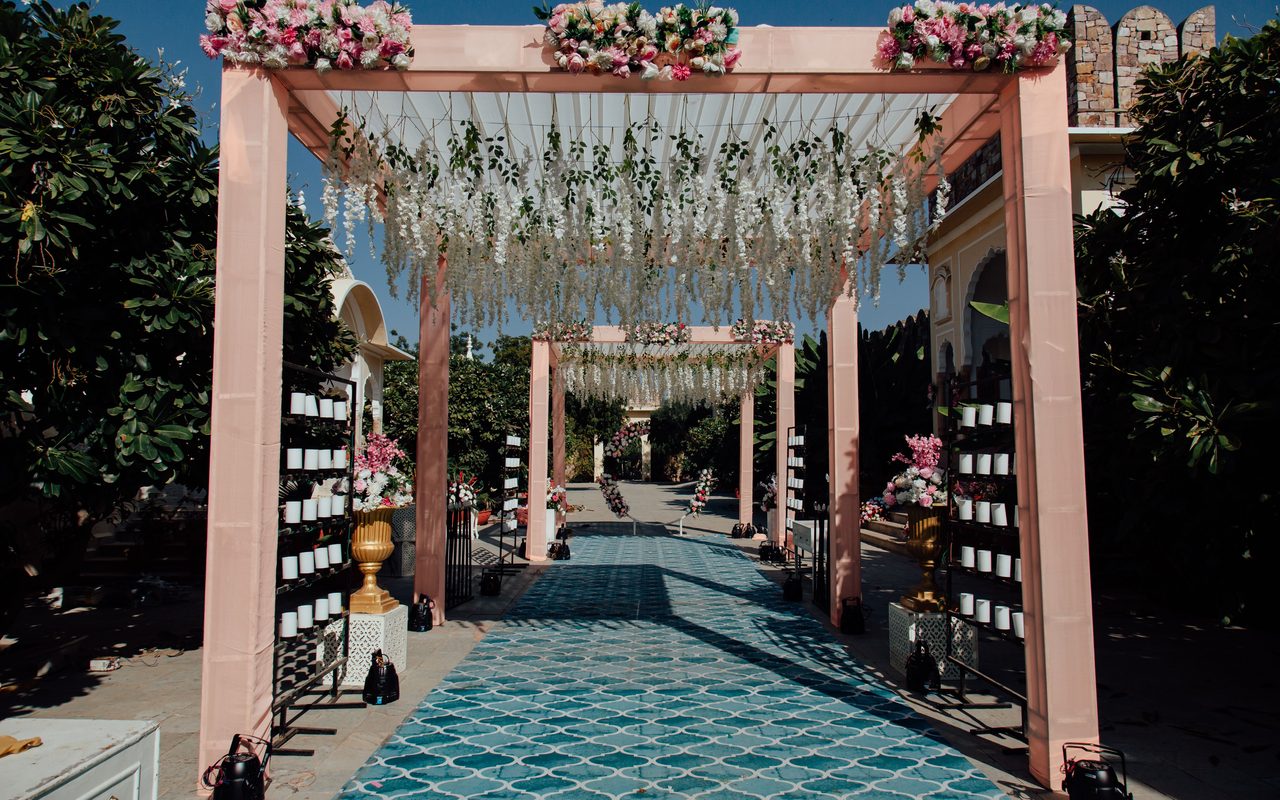 Beautiful outdoor wedding aisle with pink floral arches and a patterned path under clear sky.