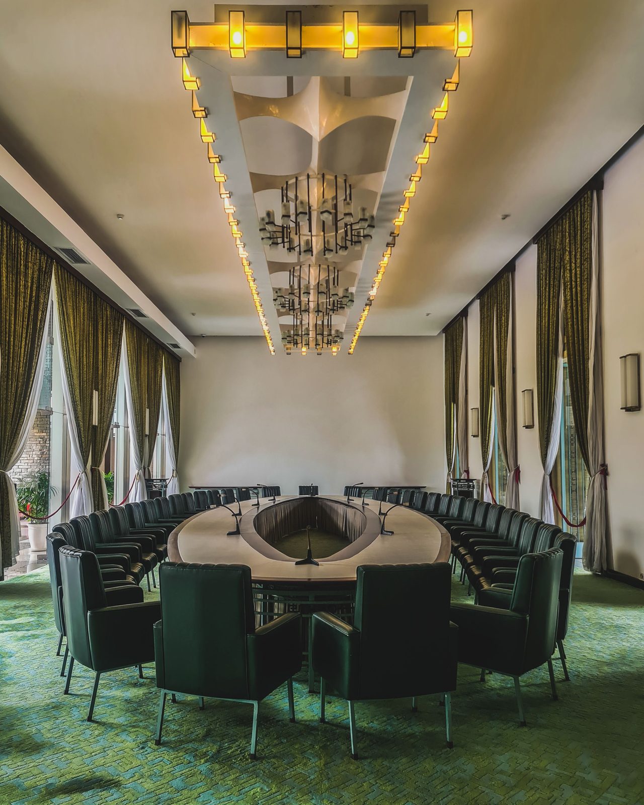 Executive boardroom with green upholstery, tall windows and a sculptural gold chandelier