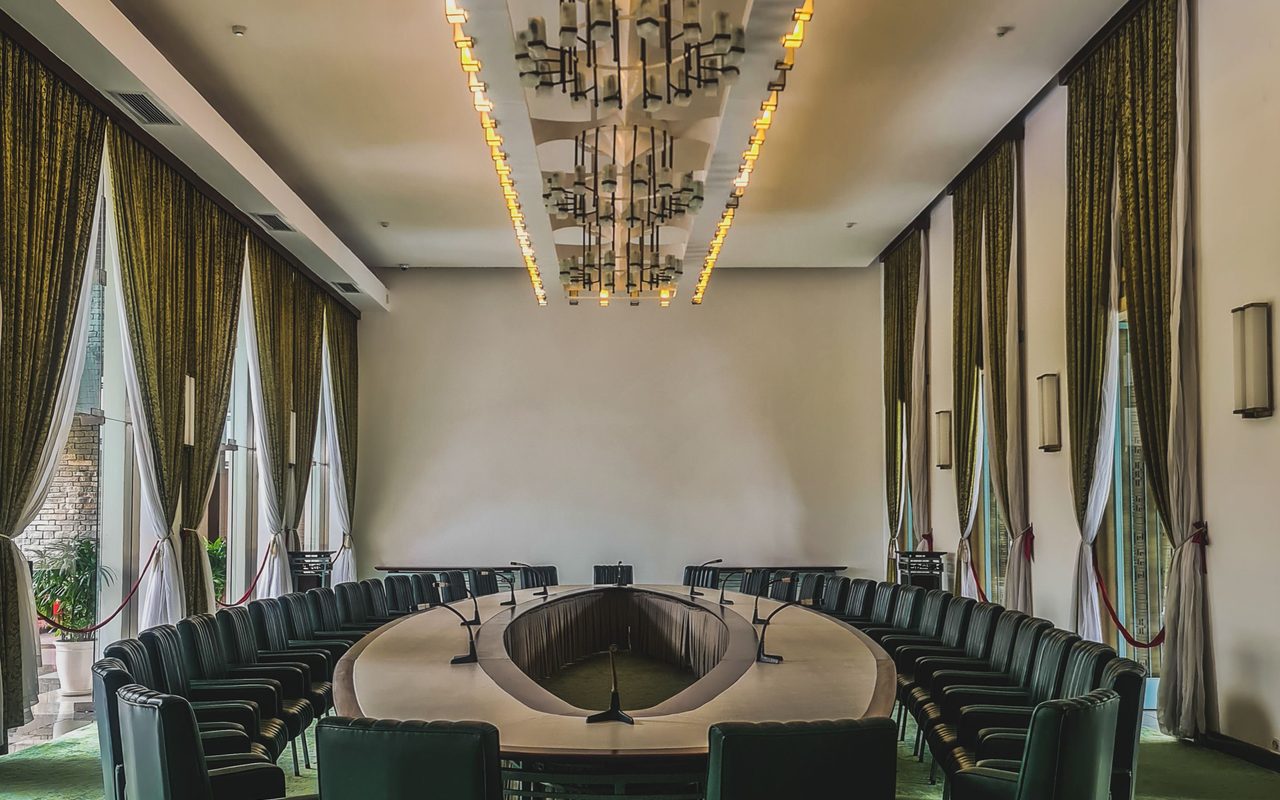 Executive boardroom with green upholstery, tall windows and a sculptural gold chandelier