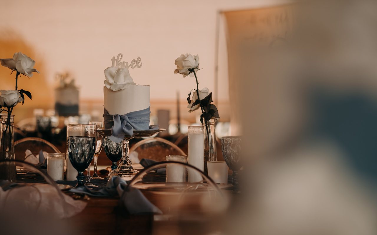 Romantic table setting with white roses, candles, and elegant glassware at a wedding reception.