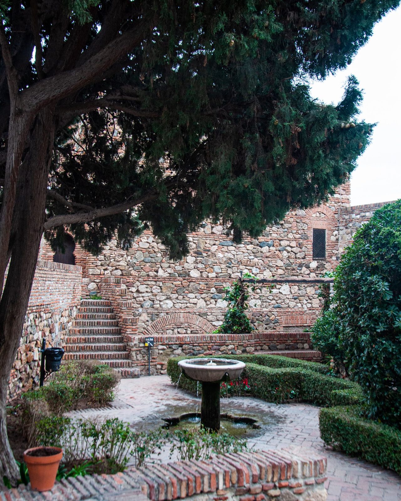 Serene courtyard with stone walls, a central fountain, and lush greenery, offering a peaceful retreat.