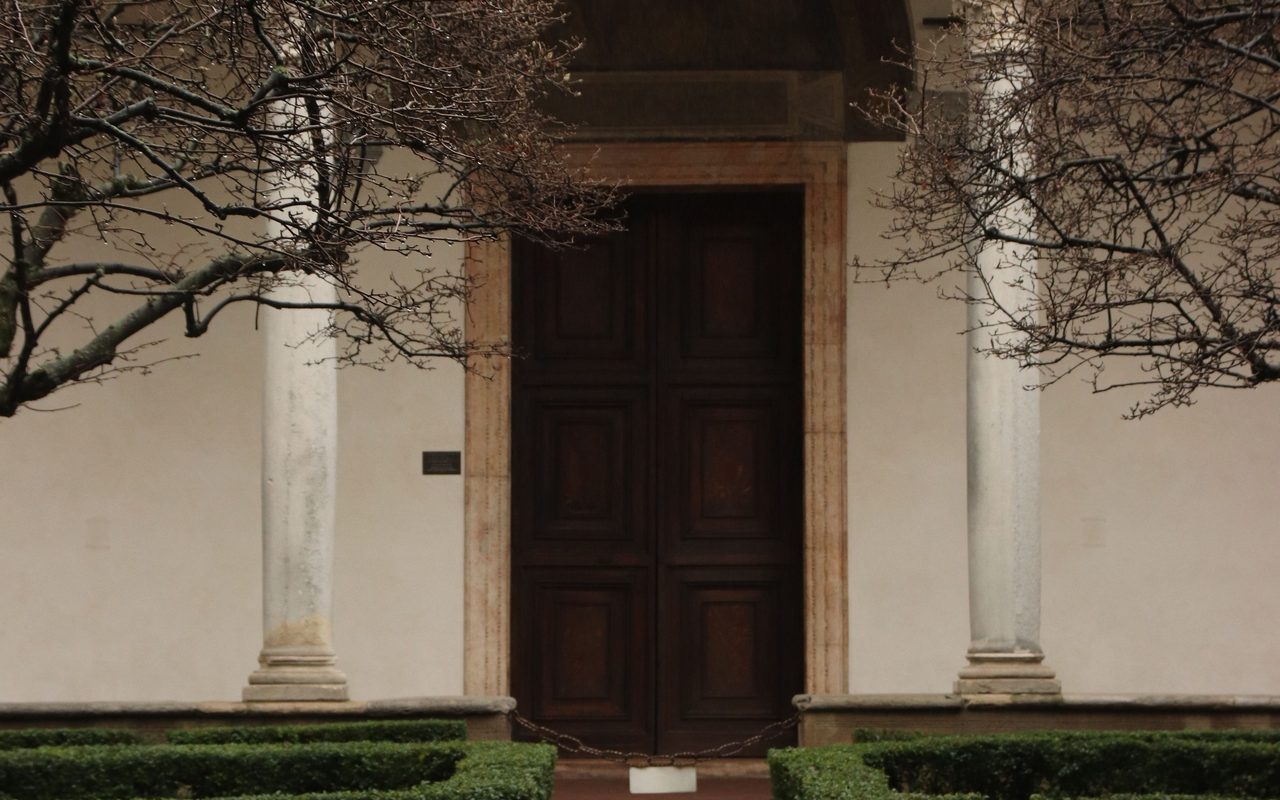 Elegant courtyard featuring a stone fountain, trimmed hedges, and an arched entrance with intricate columns.