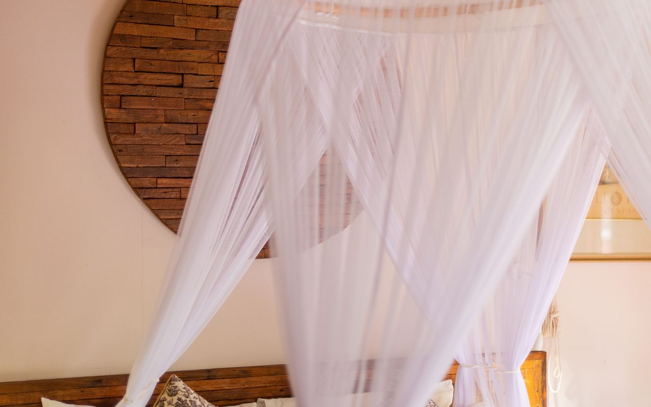 Ivory canopy, white bedding and warm wood in a softly lit suite