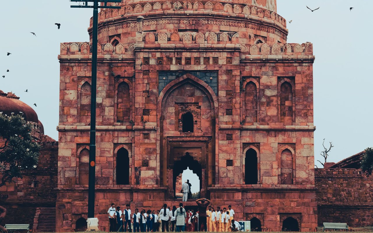 A group of people stand in front of a historic tomb in New Delhi, India, showcasing Mughal architecture.