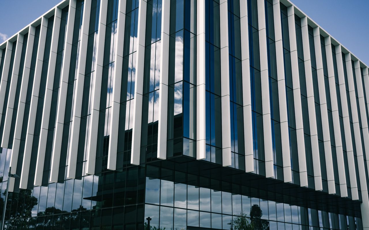 Architectural shot of a modern glass office building against a clear sky.