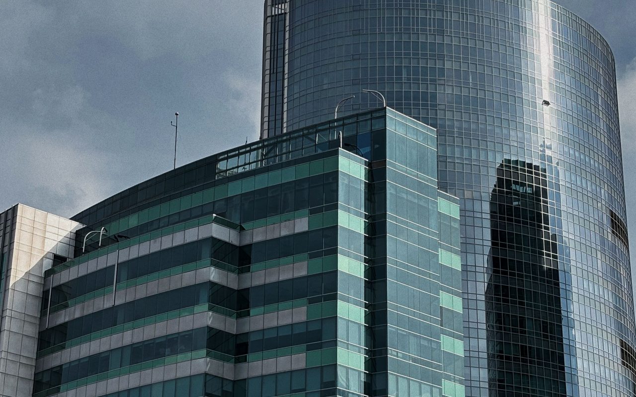 Tall office building with reflective glass, modern architecture under a cloudy sky.