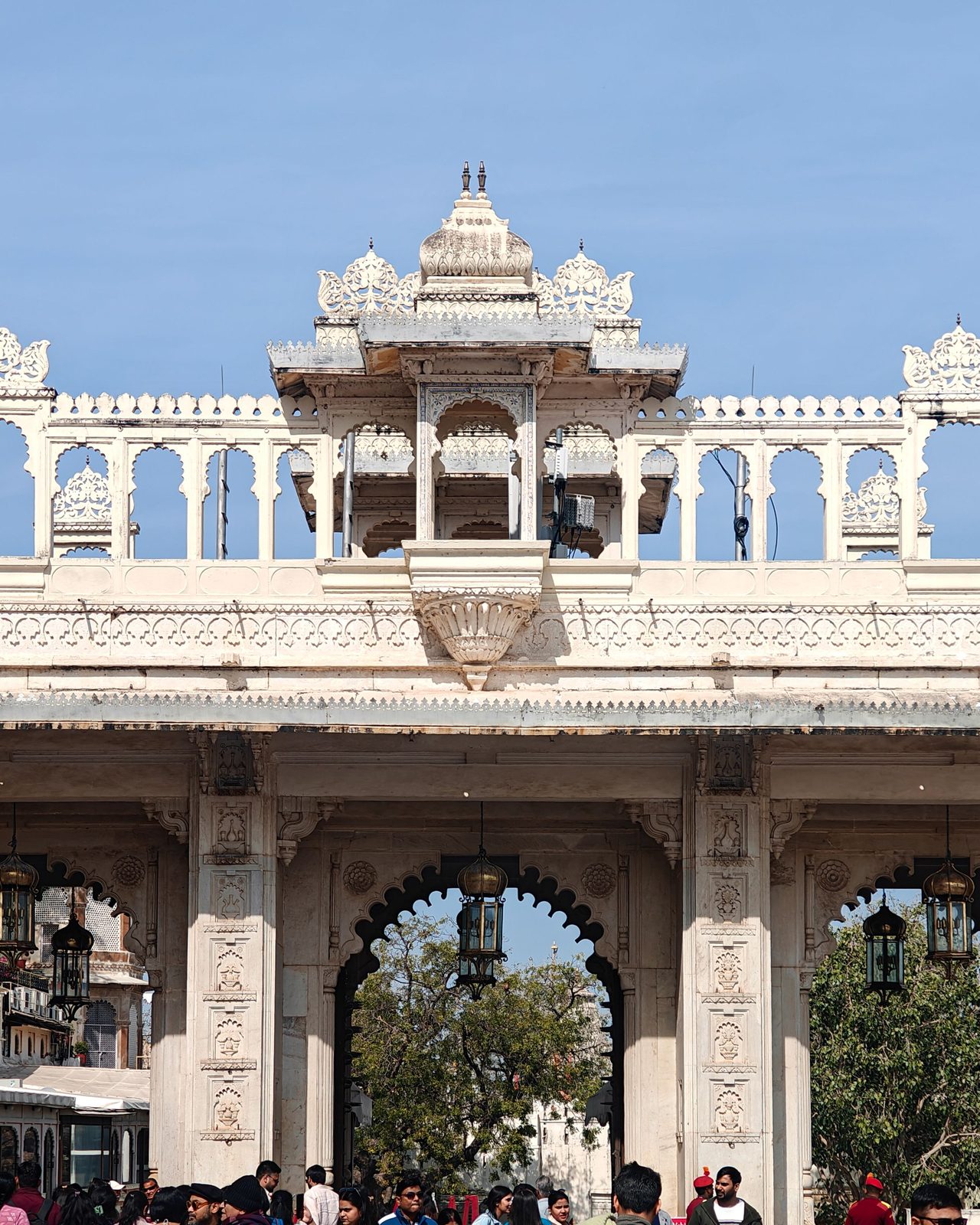 Crowds gather under the ornate gateway of Udaipur City Palace, a historic architectural gem.