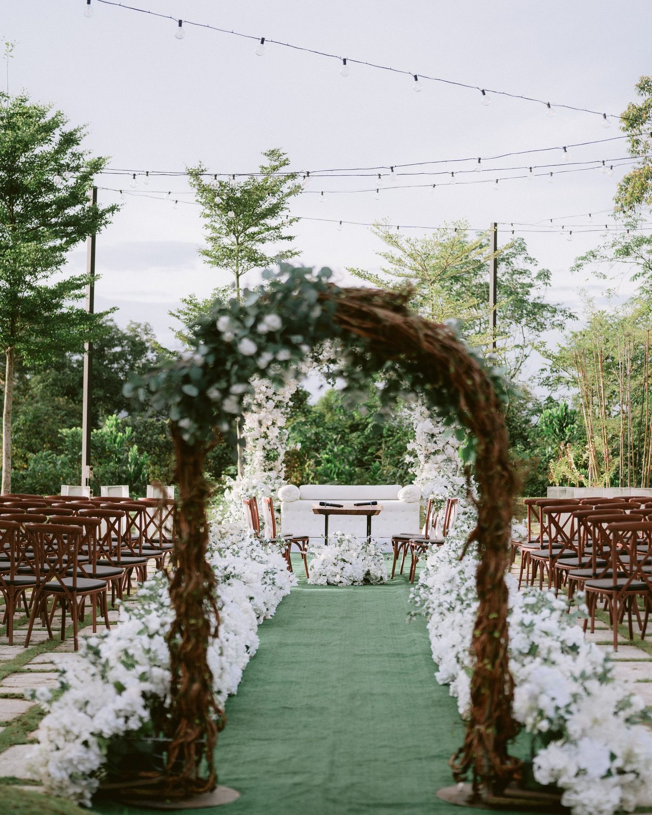 Beautiful outdoor wedding ceremony setup with archway, chairs, and lights in lush garden setting.