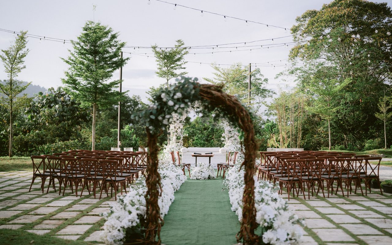 Beautiful outdoor wedding ceremony setup with archway, chairs, and lights in lush garden setting.