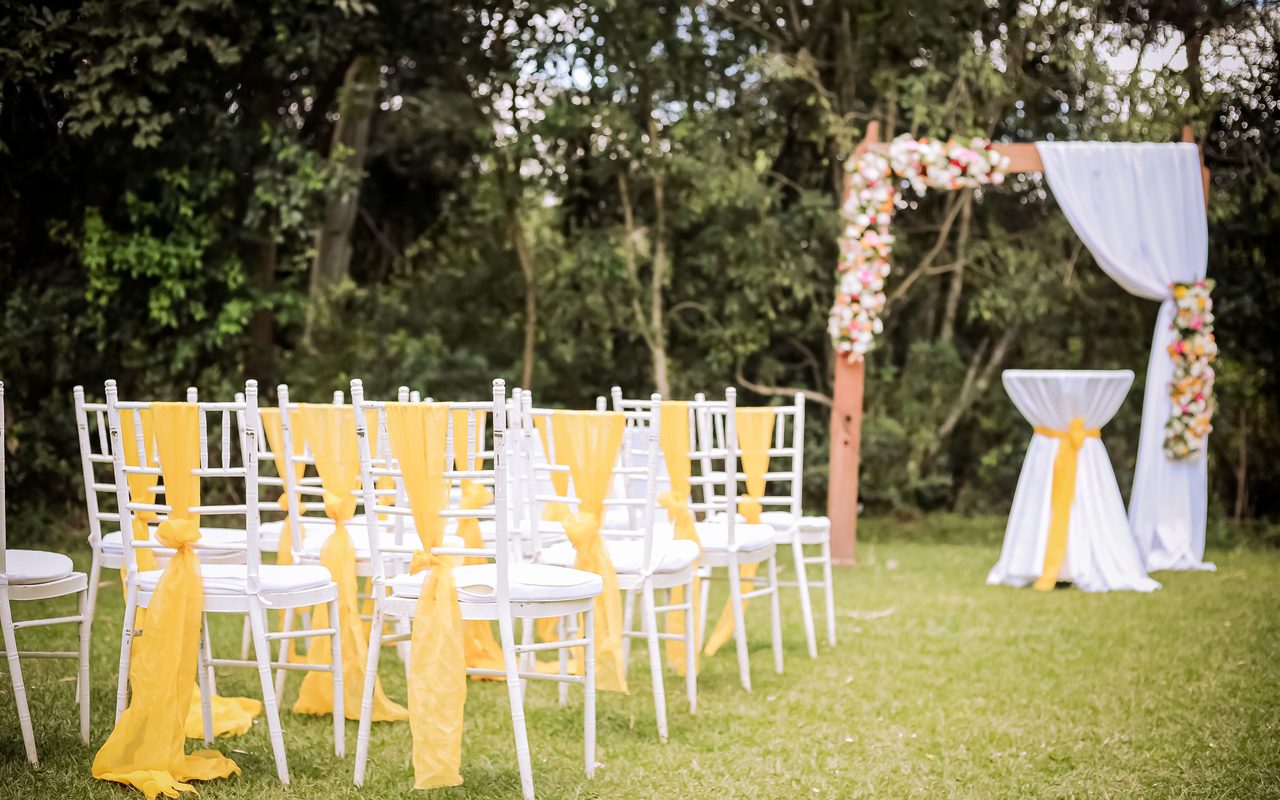 Charming outdoor wedding setup featuring a floral arch and white chairs with yellow sashes.