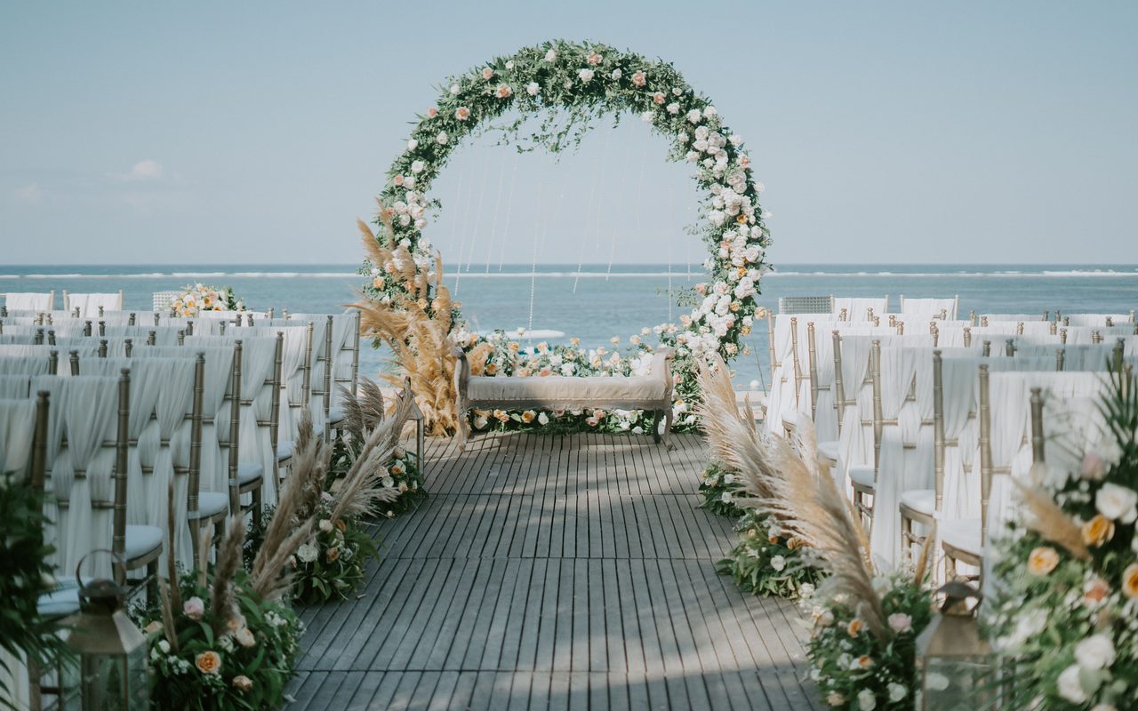 Beautiful beachside wedding setup with elegant floral arch and ocean backdrop.