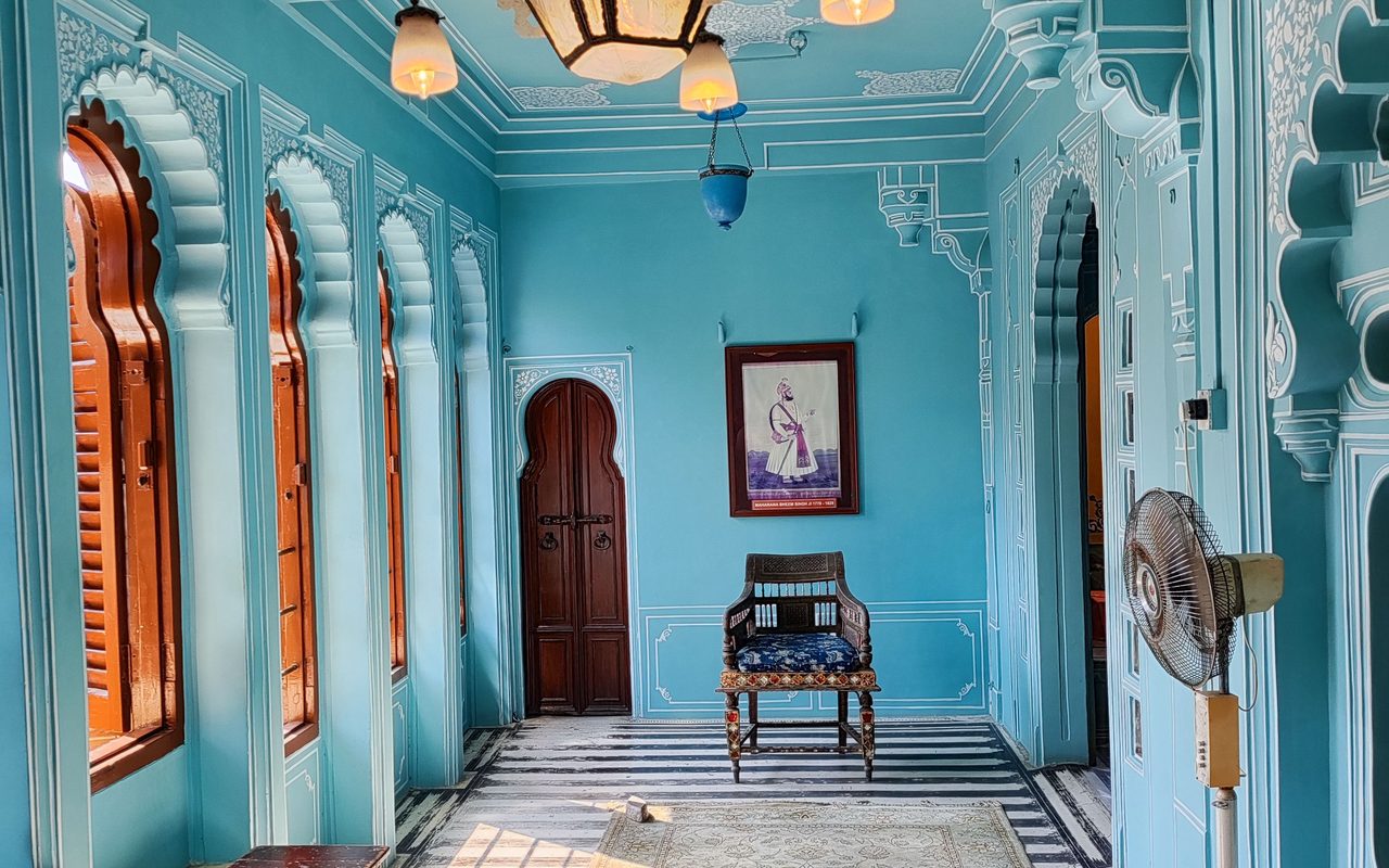 Elegant Indian palace corridor with ornate blue walls and arched windows, showcasing historic charm.