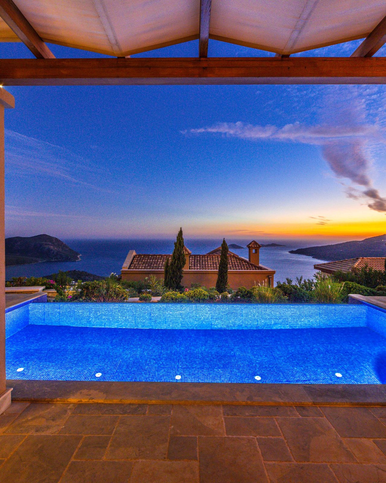 a luxury villa and infinity pool overlooking the sea at sunset.
