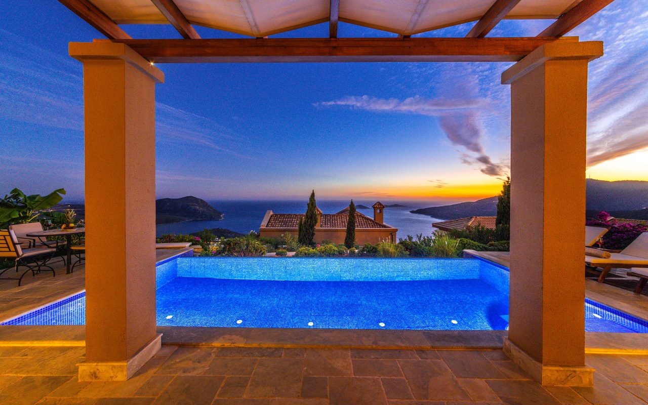 a luxury villa and infinity pool overlooking the sea at sunset.