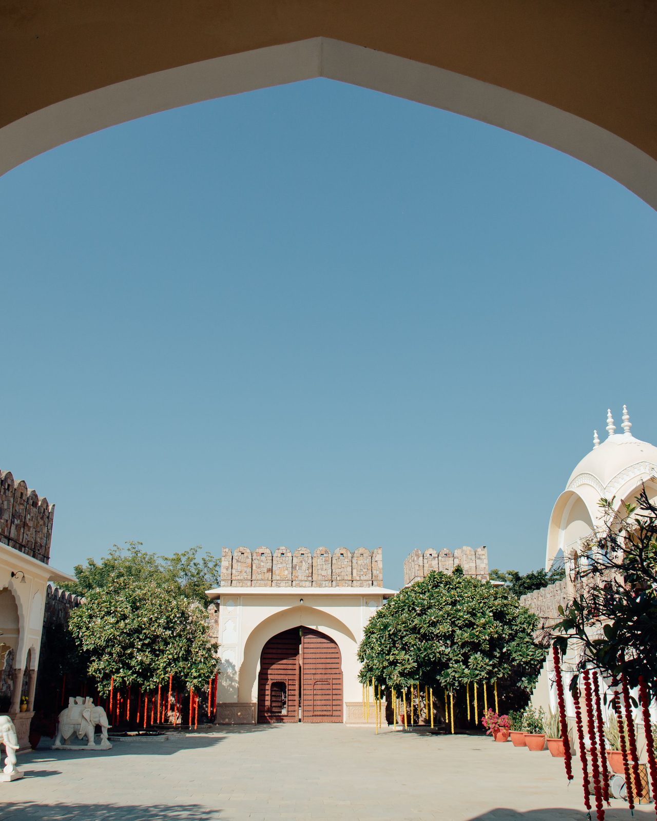 Indian architectural courtyard featuring traditional arches and vibrant gardens under a clear blue sky.