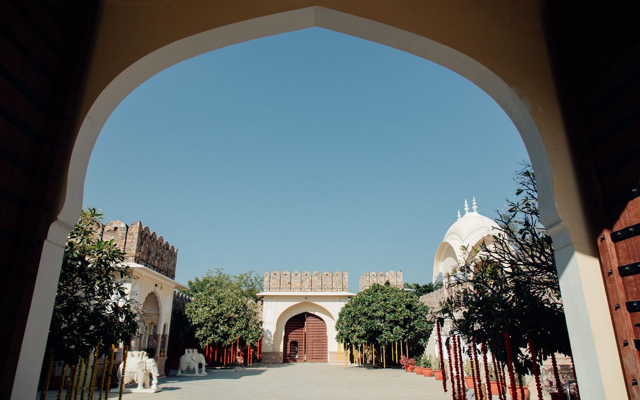 Indian architectural courtyard featuring traditional arches and vibrant gardens under a clear blue sky.