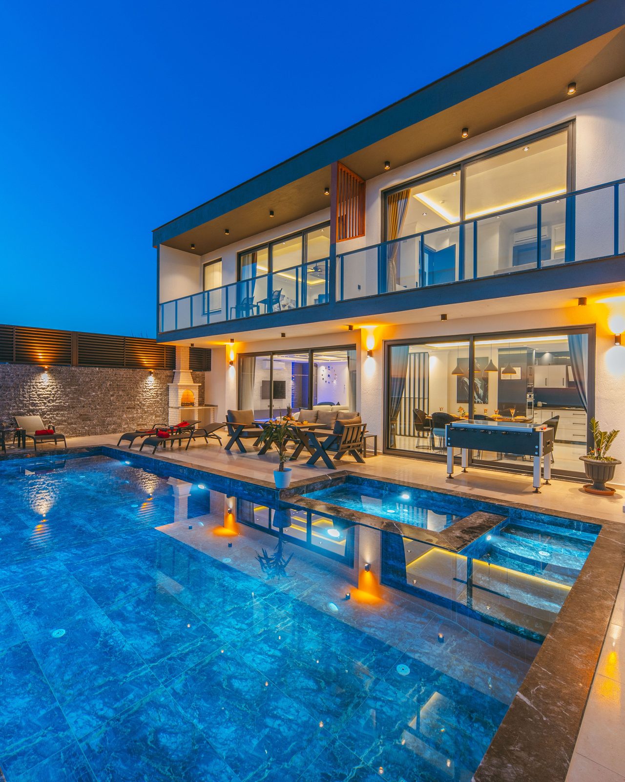 Modern luxury villa at dusk with an illuminated swimming pool and elegant terraces.