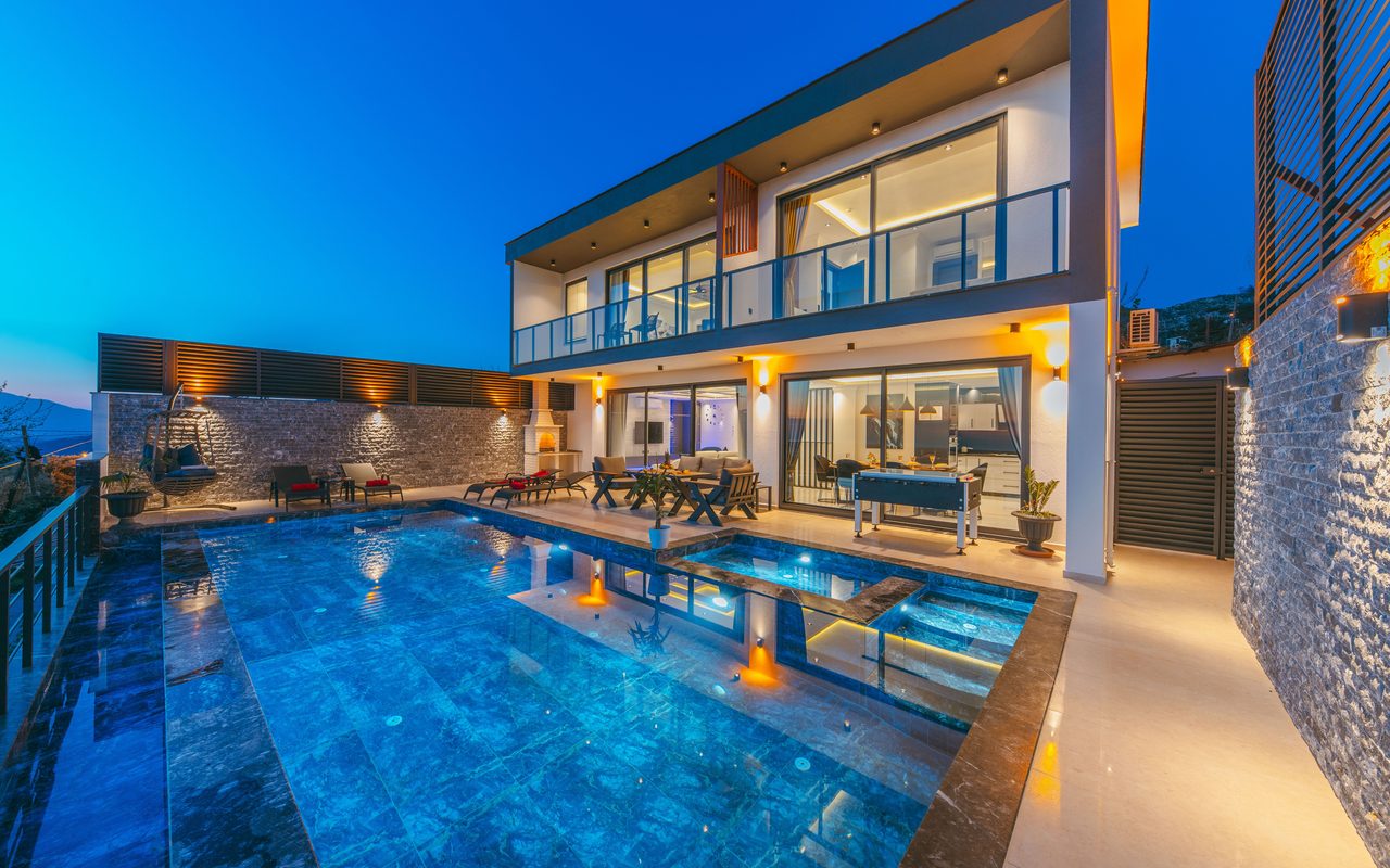Modern luxury villa at dusk with an illuminated swimming pool and elegant terraces.