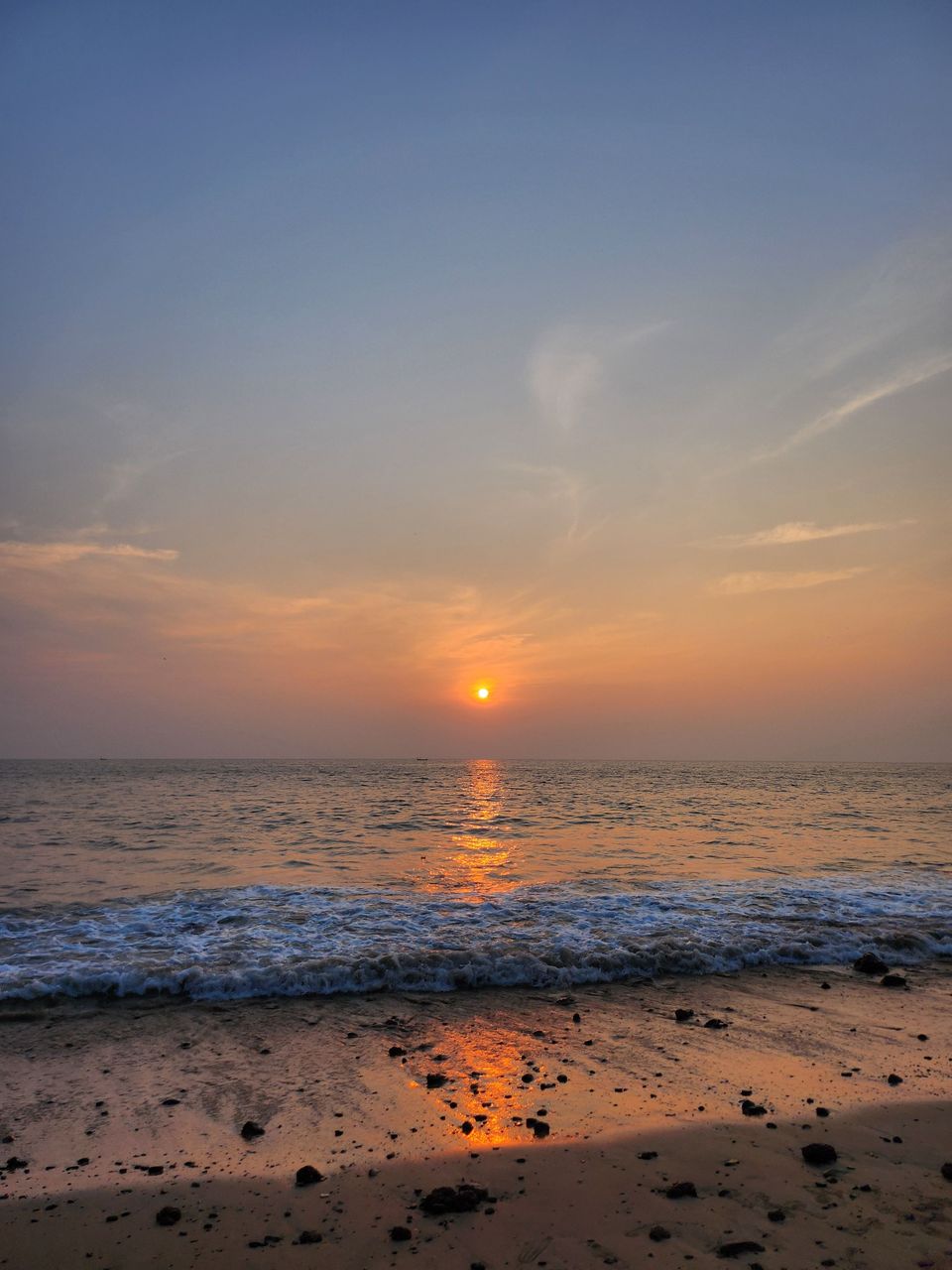 Sunset above waves washing onto a beach in Goa
