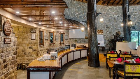 Bar and lounge with stone walls and dining tables at Infinity Resorts Corbett