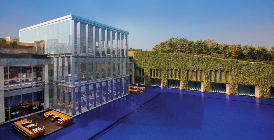 Glass pavilion beside a reflecting pool and green wall
